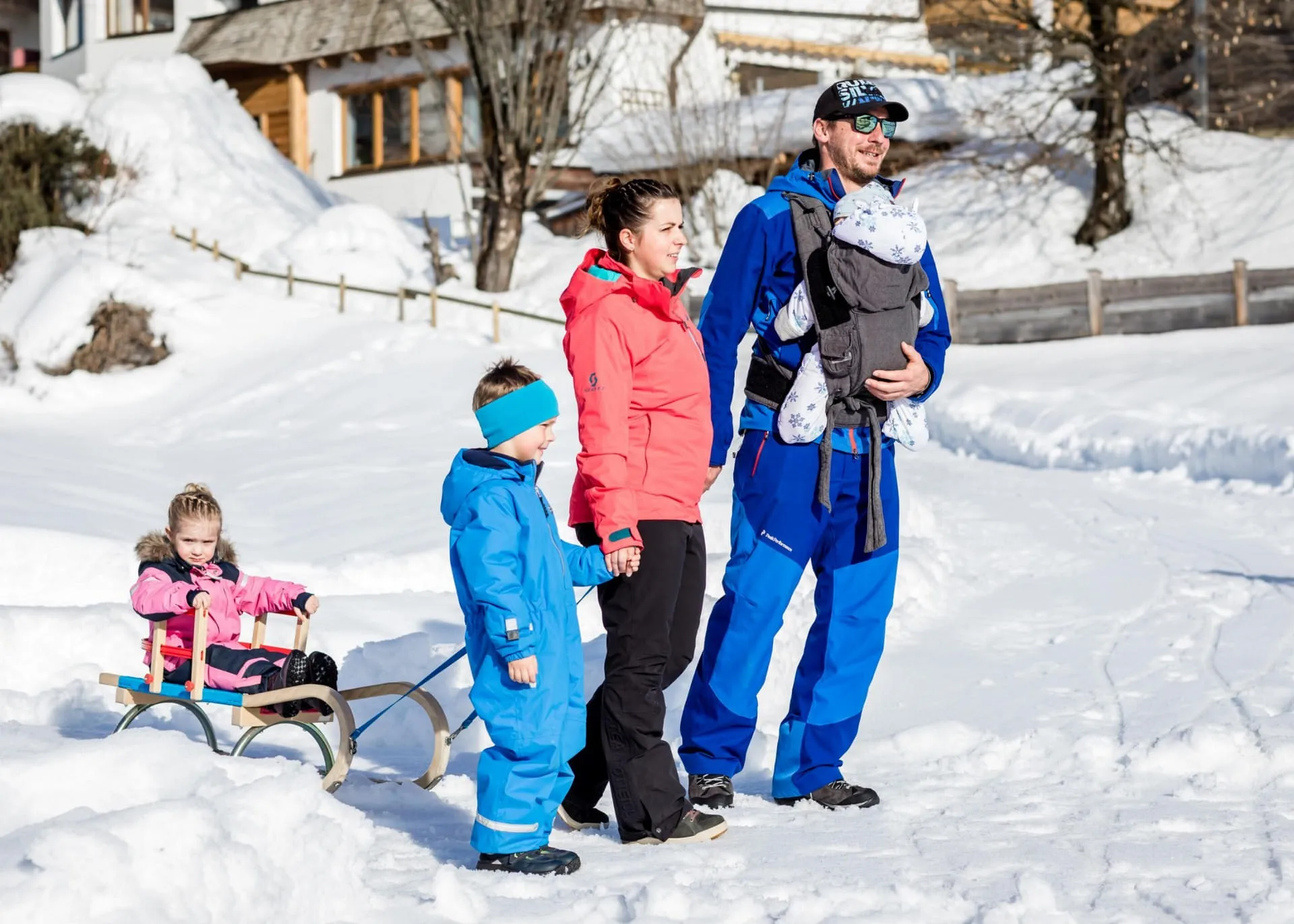 Familie mit drei Kindern beim Rodeln auf verschneiter Bahn