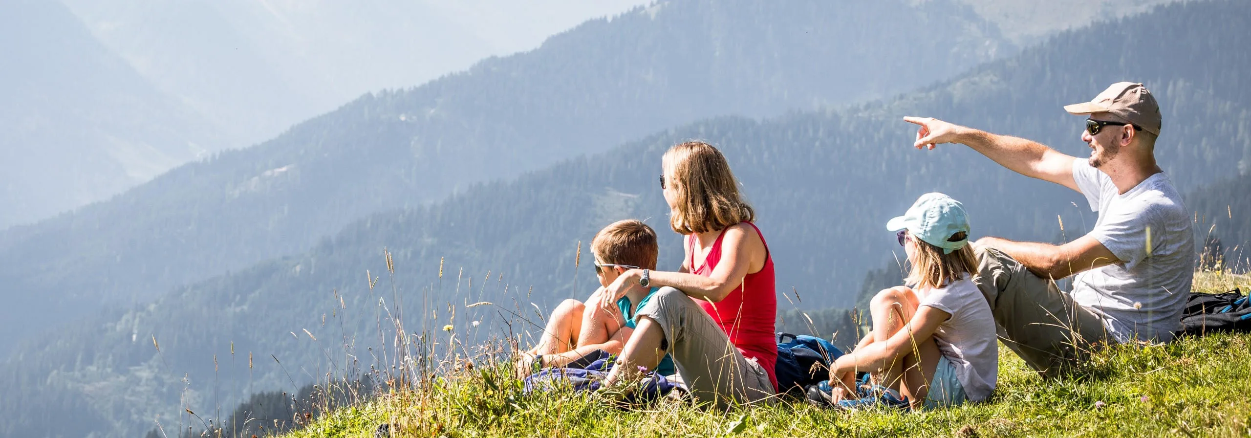 Familie sitzt auf einer Wiese und genießt den Blick auf die Berge der